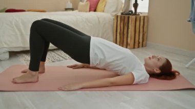 Kafkas saçlı genç kadın rahat bir yatak odası ortamında yoga yapıyor, odaklanmış ve rahatlamış..