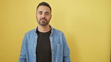 Kot gömlek giyen genç, hispnanik bir adam, şaşırmış duruyor, ağzı açık bir şekilde şaşkınlık dolu bir ifade sergiliyor. izole edilmiş, sarı arkaplan üzerine kurulur.