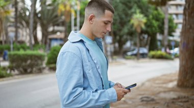 Genç bir İspanyol adam, şehir sokağında telefonuna bakarken açık havada bir bağlantı hissi uyandırıyor..