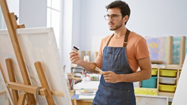 Sanat stüdyosundaki tuvale önlük takmış, sakallı yakışıklı İspanyol bir adam.