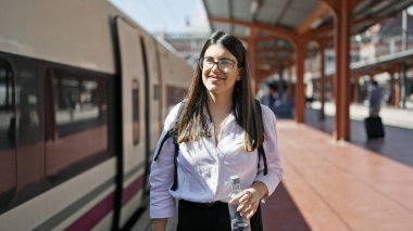 Genç ve güzel İspanyol kadın tren istasyonunda elinde bir şişe suyla demiryolunda yürüyor.