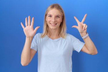 Kafkasyalı genç bir kadın günlük mavi tişört giyer ve 8 numaralı parmaklarıyla onu gösterirken kendinden emin ve mutlu bir şekilde gülümser.. 