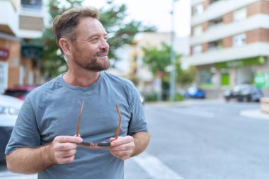 Middle age man smiling confident holding sunglasses at street