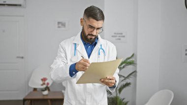 Bearded man in lab coat reviewing documents in a modern clinic's waiting area. clipart