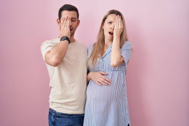 Genç bir çift pembe arka planda duran bir bebek bekliyor. Yarı yüz, göz ve ağzı elle kapatmaktan yoruluyorlar. Yüzüm acıyor.. 