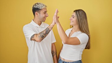 Güzel çift gülümsüyor, kendinden emin beşlik çakıyor izole edilmiş sarı arka planda kutlama yapıyorlar.