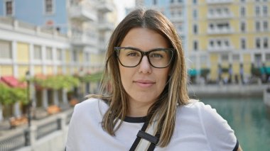 Renkli binaların önünde gözlüklü esmer bir kadının portresi ve Doha, Katar 'da su kanalı..