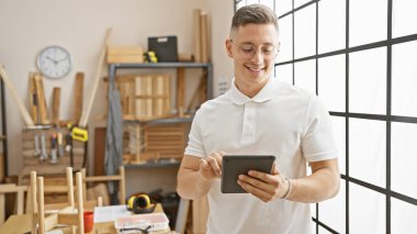 İyi donanımlı bir marangoz atölyesinde tablet kullanan yakışıklı bir genç..