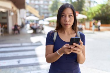 Young asian woman using smartphone with serious expression at street