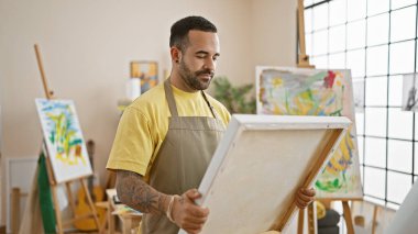 Odaklanmış bir İspanyol, tablosunu parlak bir sanat stüdyosunda inceliyor..