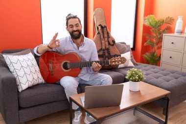 Sakallı İspanyol bir adam evde klasik gitar çalıyor. Parmaklarıyla işaret veriyor, gülümsüyor. Mükemmel bir sembol. 