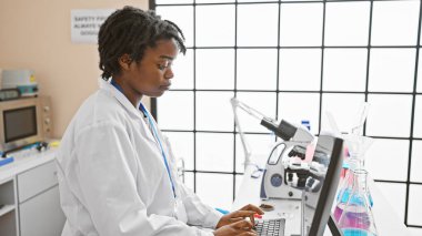 Genç Afrikalı Amerikalı kadın bilim adamı laboratuvarda, kapalı alanda bilgisayar üzerinde çalışıyor..