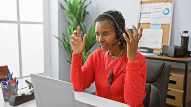 Modern bir ofis ortamında video görüşmesinde kulaklık takan Afrikalı Amerikalı bir kadın..