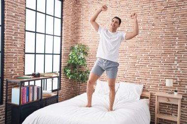 Young hispanic man smiling confident dancing on bed at bedroom