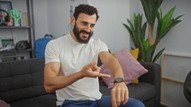 Gülümseyen sakallı adam modern oturma odasında akıllı adamı kontrol ediyor.