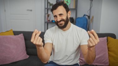 Gülümseyen sakallı adam rahat bir oturma odasında para hareketi yapıyor, kendine güven ve rahatlık yansıtıyor..