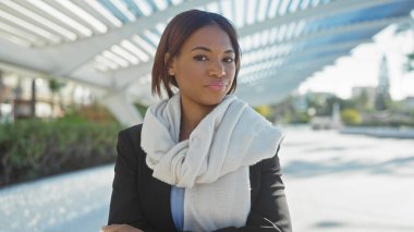 African american woman in business attire poses confidently outdoors in a modern city park setting during the daytime. clipart