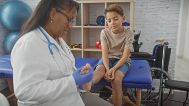 Bir kadın terapist, bir erkeğin ayağını fizik tedavi kliniğinin rehabilitasyon odasında muayene ediyor. Çocuk sağlığı seti öneriyor..