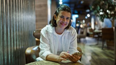 Kafeteryada gülümseyen akıllı telefon kullanan güzel bir İspanyol kadın.