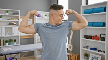 Modern bir rehabilitasyon kliniğinin terapi odasında gururla kaslarını esneten mutlu genç bir İspanyol..