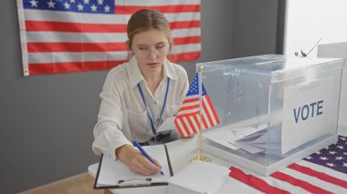 Gözlüklü, odaklanmış genç bir kadın, Amerikan bayrağı ve oy sandığıyla birlikte bir seçim merkezinde not alıyor..