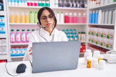 Eczanede çalışan genç bir Arap kadın dizüstü bilgisayar kullanan şüpheci ve gergin kollarını kavuşturarak yüzünü tasvip etmeyen bir ifade kullanıyor. negatif kişi. 