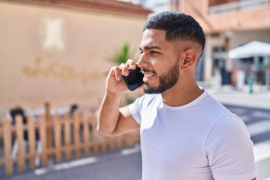 Genç Latin adam gülümsüyor. Kendine güveniyor. Akıllı telefondan konuşuyor.