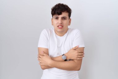 Gündelik beyaz tişört giyen, kış soğuğu için titreyen ve soğuktan donan, yüzünde üzgün ve şok ifadesi olan genç bir adam. 