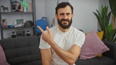 Kafası karışmış sakallı bir adam modern oturma odasını işaret ediyor..