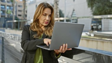 Modern bir şehir ortamında dizüstü bilgisayar kullanan odaklanmış bir İspanyol iş kadını..