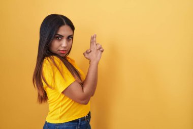 Sarı arka planda duran genç Arap kadın sembolik bir silahla el hareketleriyle cinayet silahlarıyla oynuyor, kızgın surat. 