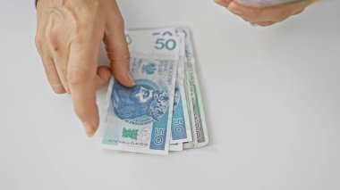 A mature woman counts polish zloty banknotes against a white background, indicating finance management and savings. clipart