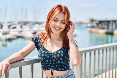 Genç, beyaz bir kadın Balustrade 'a yaslanmış deniz kenarına bakıyor.