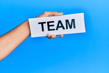 Hand of caucasian man holding paper with team word over isolated blue background