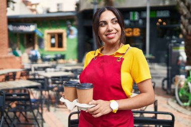 Young beautiful arab woman waitress smiling confident holding take away coffee at coffee shop terrace