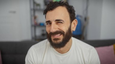 Evde sakallı, gülümseyen, orta yaşlı bir adam rahat bir ortamda olgun ve çekici bir cazibe yayıyor..