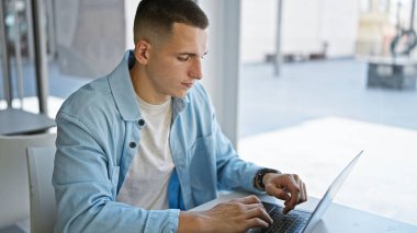 Parlak bir üniversite kütüphanesinde dizüstü bilgisayar kullanan odaklanmış genç bir İspanyol..