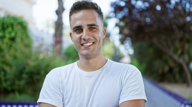 Açık hava parkında gülümseyen neşeli, genç İspanyol bir adam doğal ve rahat bir şehir yaşam tarzını canlandırıyor..
