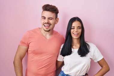 Pembe arka planda duran genç İspanyol çift kameraya seksi bir ifadeyle, neşeli ve mutlu bir yüzle bakıyor.. 
