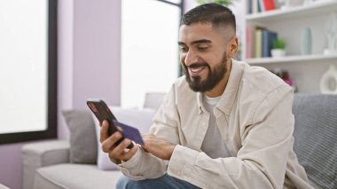 Gülümseyen adam evden online alışveriş için kredi kartı ve akıllı telefon kullanıyor.