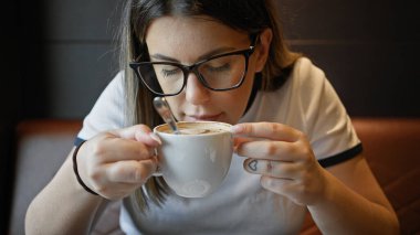 Latin kökenli yetişkin bir kadın rahat bir kafede kahve içip şık gözlük ve günlük kıyafetlerini sergiliyor..