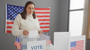 Orta yaşlı İspanyol bir kadın, arka planda Amerikan bayrağı olan bir Amerikan seçim merkezinde oy kullanıyor..