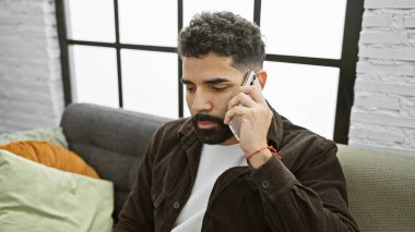 Modern bir apartman dairesinde sakallı, akıllı telefondan konuşan yakışıklı bir İspanyol..