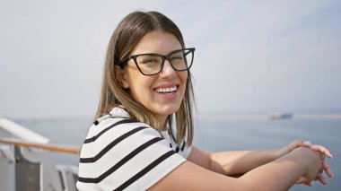 Gözlüklü gülümseyen genç bir kadın güneşli bir günde deniz seyahatinin tadını çıkarıyor..