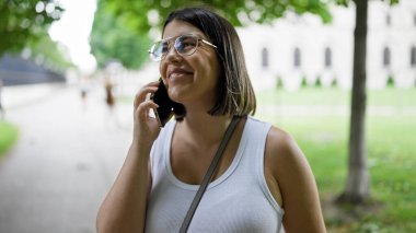 Genç ve güzel İspanyol kadın gülümsüyor mutlu bir şekilde Viyana 'daki parkta telefonda konuşuyor.