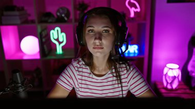 Gece karanlık bir oyun odasında kulaklıklı esmer bir kadın. Pembe ışıklarla aydınlatılmış..