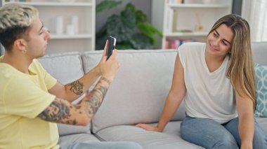 Kanepede oturan güzel bir çift evde akıllı telefondan fotoğraf çekiyor.