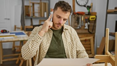 Marangozluk atölyesinde telefonla konuşan düşünceli bir İspanyol. Etrafı aletler ve ahşap işçiliğiyle çevrili..