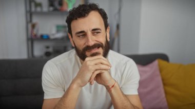 Yakışıklı, sakallı, rahat bir kanepede rahat bir oturma odasında gülümseyen olgun bir adam.
