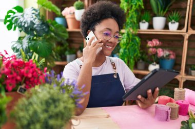 Çiçekçide dokunmatik ped kullanarak akıllı telefondan konuşan Afrikalı Amerikalı kadın çiçekçi.